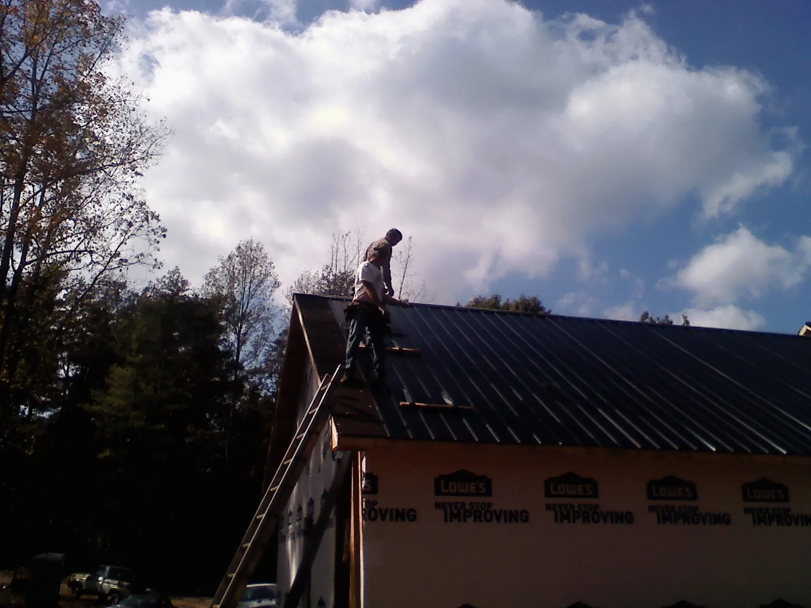 Roofer fastening dark metal panels high against a cloudy sky, from a Roof Inspection job in Templeton
